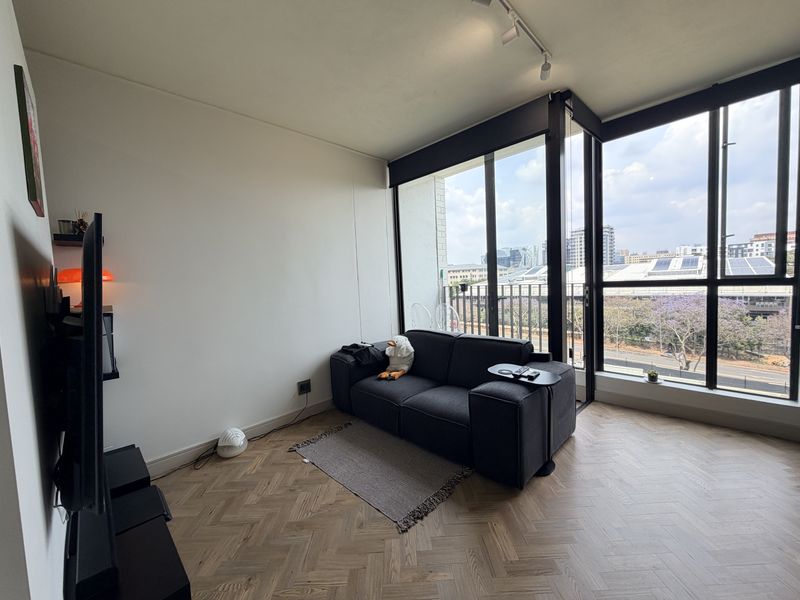 Modern living room featuring elegant herringbone timber flooring, floor-to-ceiling windows with black frames, and contemporary track lighting, offering an airy and bright atmosphere.