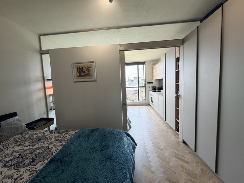 Modern open-plan apartment featuring herringbone timber flooring, sleek built-in cabinetry, and a sliding partition wall separating the bedroom from the kitchen area.