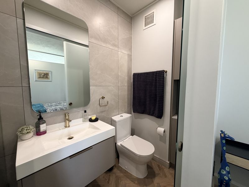 Modern bathroom featuring a wall-mounted vanity with integrated basin, brass fixtures, large mirror, and elegant large-format wall tiles with herringbone flooring.