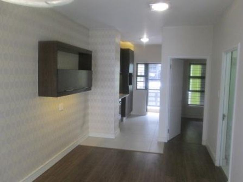 An open-plan living area featuring a mix of laminate and tiled flooring, built-in wall shelving, and neutral finishes throughout the apartment.