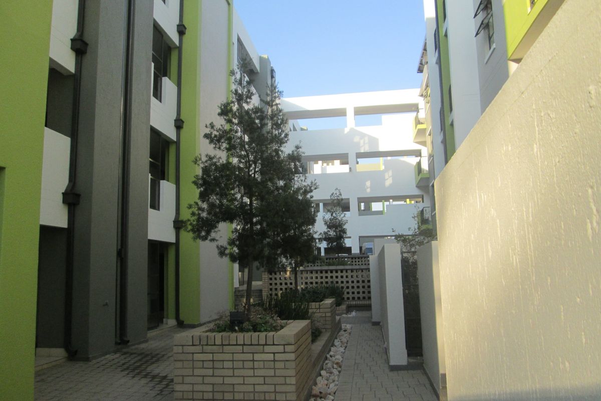 A view of the paved courtyard area between apartment blocks, featuring brick planter boxes and modern multi-story building facades.