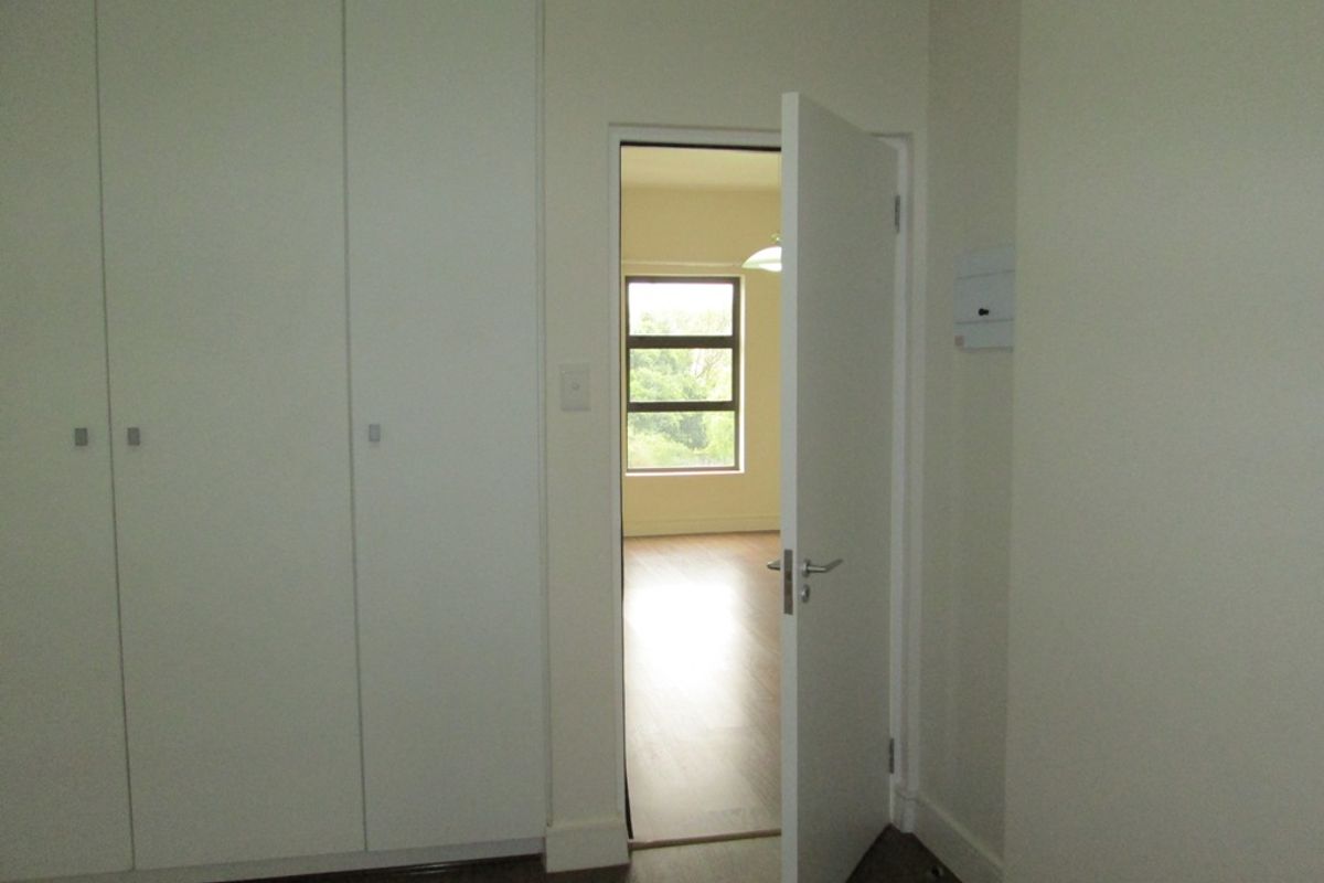 A clean, empty bedroom featuring built-in cupboards, laminate flooring, and a doorway leading to an adjacent room with natural light.