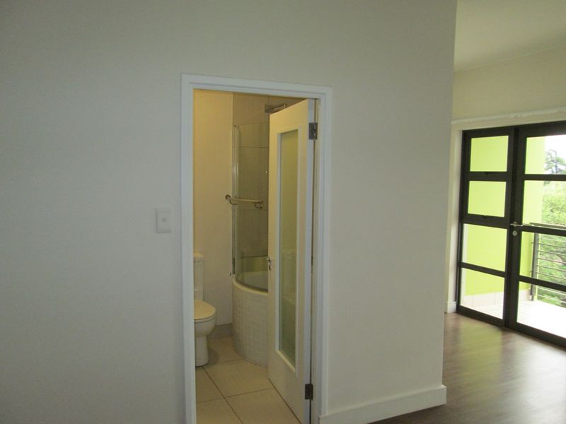 A view into a compact bathroom featuring a shower enclosure and toilet, accessible from an adjacent living area with balcony access.