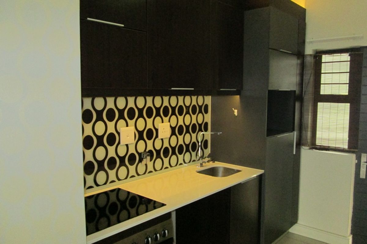 Compact kitchen featuring dark cabinetry, a modern electric hob, a stainless steel sink, and a distinctive patterned tiled backsplash.