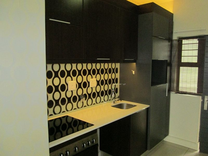 Compact kitchen featuring dark cabinetry, a modern electric hob, a stainless steel sink, and a distinctive patterned tiled backsplash.