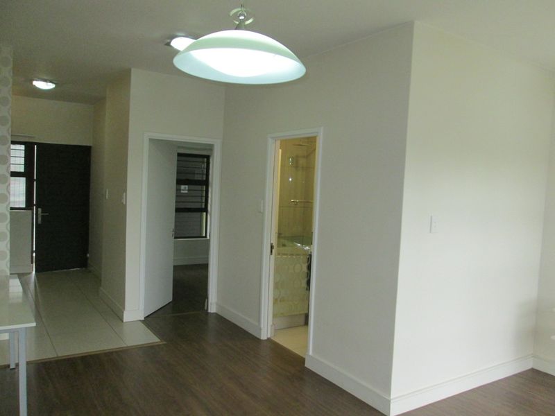 A bright, empty hallway featuring a mix of laminate and tiled flooring, leading to multiple rooms with modern lighting fixtures.