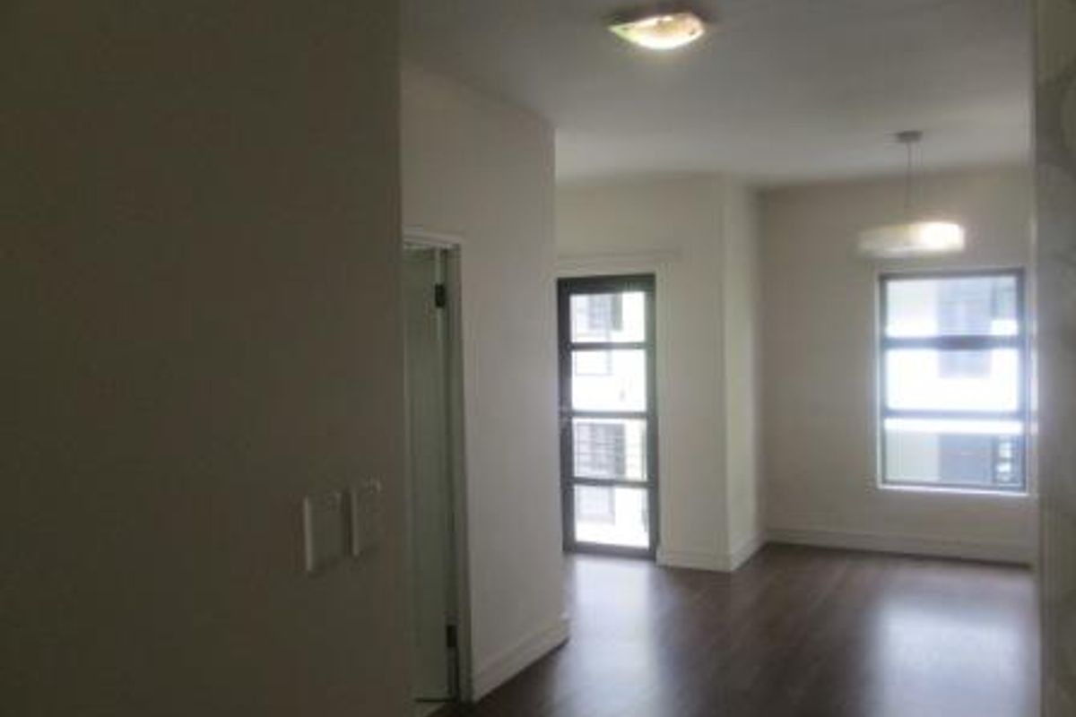 A bright, empty living area featuring dark laminate flooring, modern lighting fixtures, and a glass panel door leading to an outdoor space.