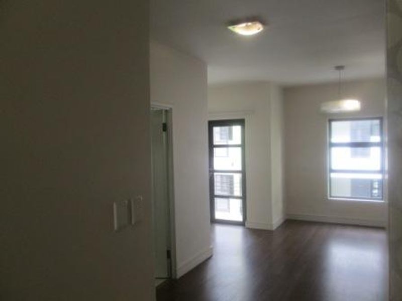 A bright, empty living area featuring dark laminate flooring, modern lighting fixtures, and a glass panel door leading to an outdoor space.