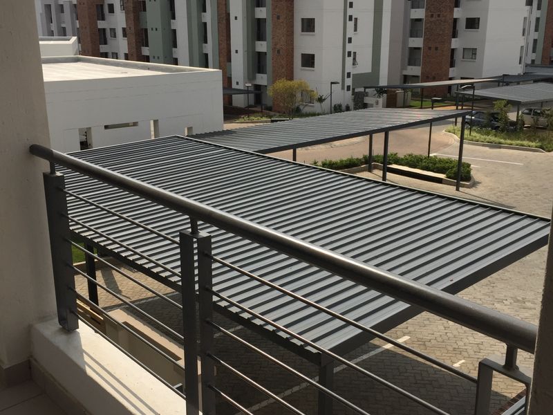 A view from a balcony overlooking the apartment complex parking area with metal carport structures and paved driveways.