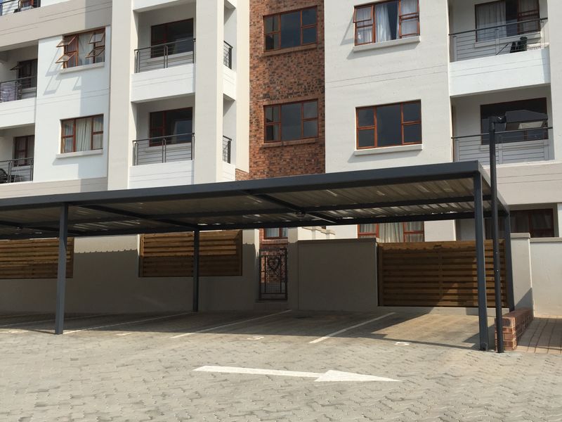 Exterior view of a modern apartment complex featuring a paved driveway with covered parking bays and multi-story residential units with balconies.