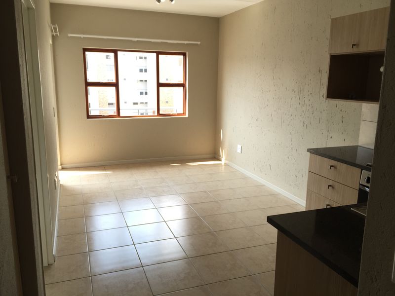 An open-plan living and kitchen area featuring tiled floors, built-in cabinetry with granite countertops, and a large window providing natural light.