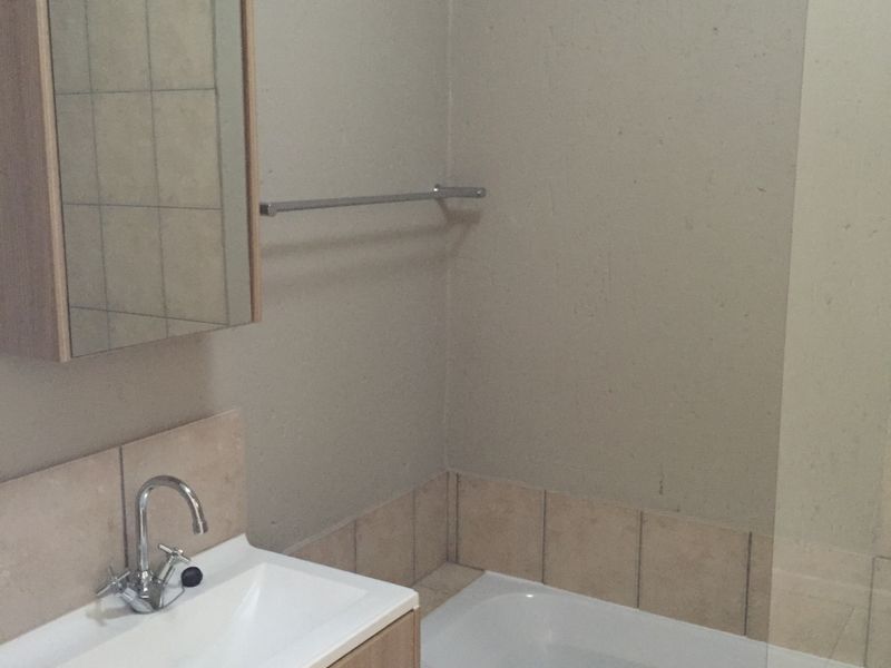 A functional bathroom featuring a vanity with basin, medicine cabinet, and a bathtub with a glass shower screen and tiled splashback.