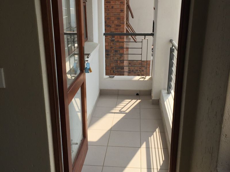 A compact, tiled balcony featuring a metal balustrade and accessible via a timber-framed glass door, offering a functional outdoor space.