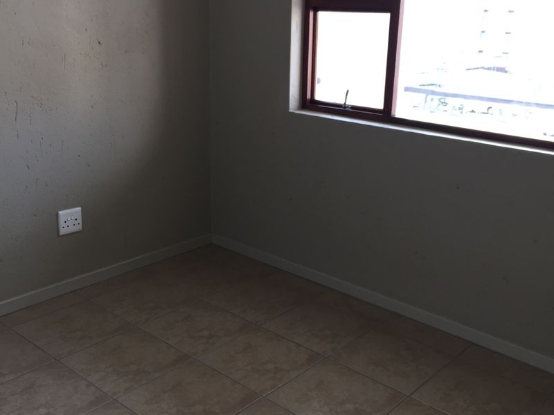 An empty bedroom featuring tiled flooring and a window with a brown frame, requiring minor cosmetic updates to the wall finishes.