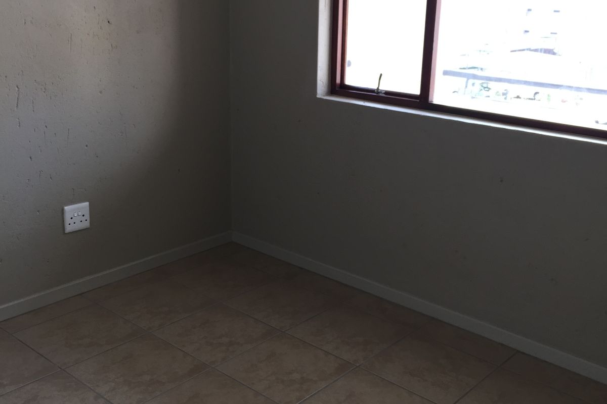 An empty bedroom featuring tiled flooring and a window with a brown frame, requiring minor cosmetic updates to the wall finishes.