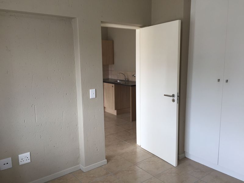 A clean, empty bedroom featuring built-in cupboards, tiled flooring, and a doorway leading to a kitchen area.