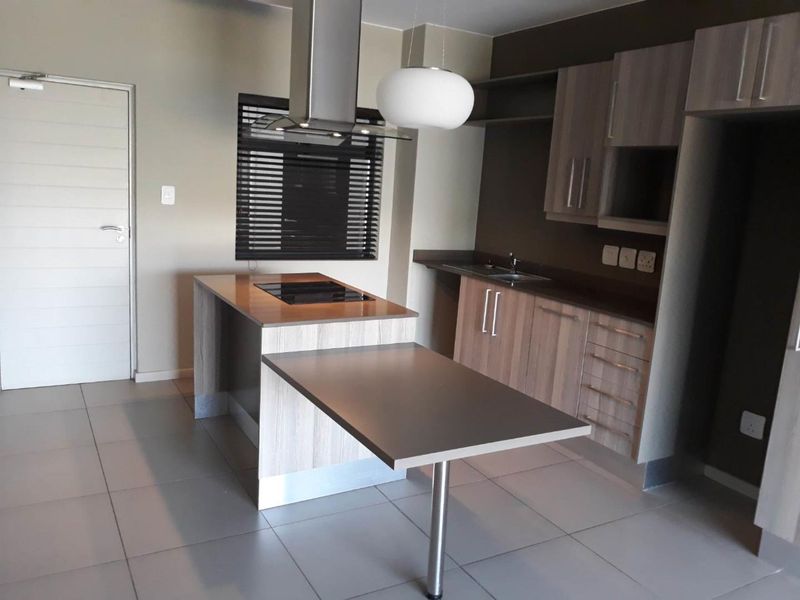 Modern kitchen featuring a central island with integrated cooktop, ample cabinetry, stainless steel extractor fan, and neutral tiled flooring.