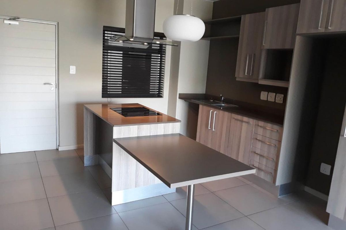 Modern kitchen featuring a central island with integrated cooktop, ample cabinetry, stainless steel extractor fan, and neutral tiled flooring.