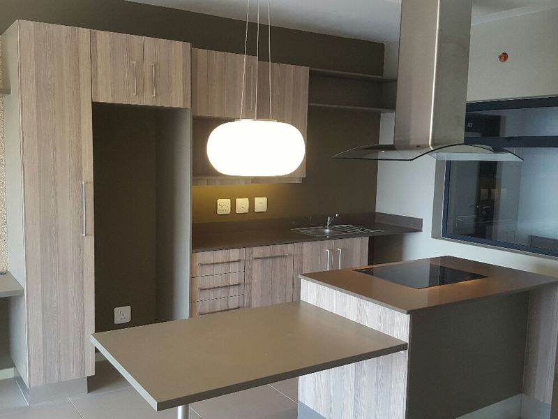 Modern kitchen featuring wood-grain cabinetry, a central island with a cooktop, stainless steel extractor fan, and integrated sink area.