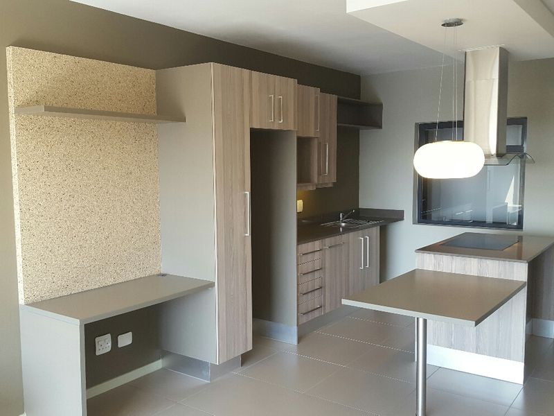 Modern kitchen featuring light wood-grain cabinetry, a breakfast bar, integrated hob, extractor fan, and neutral tiled flooring in an open-plan layout.