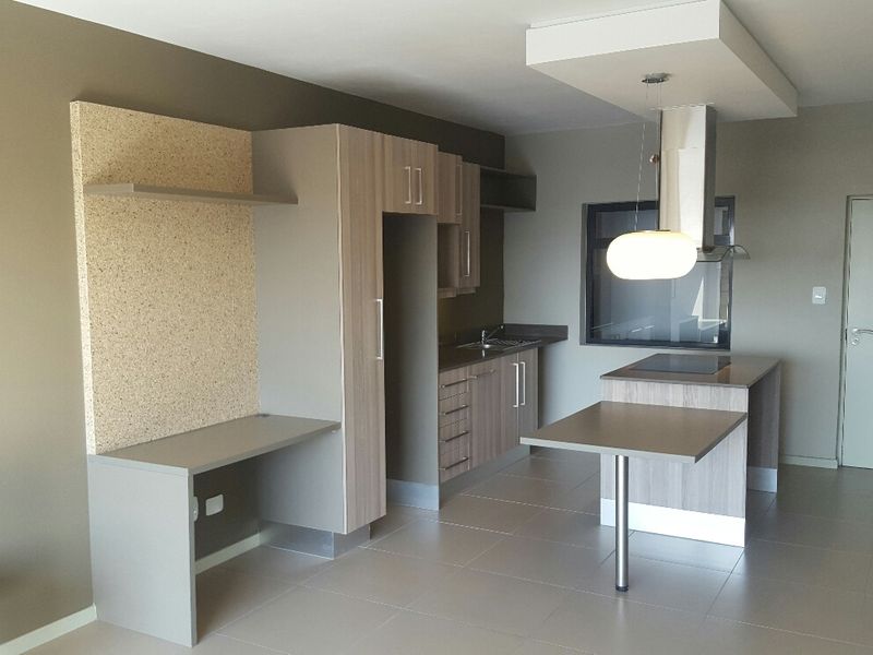 Modern open-plan kitchen featuring sleek cabinetry, integrated hob, extractor fan, and a convenient built-in desk area with neutral tiled flooring throughout.
