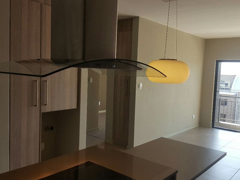 Open-plan kitchen and living area featuring modern cabinetry, built-in hob, extractor fan, and access to a private balcony through sliding glass doors.