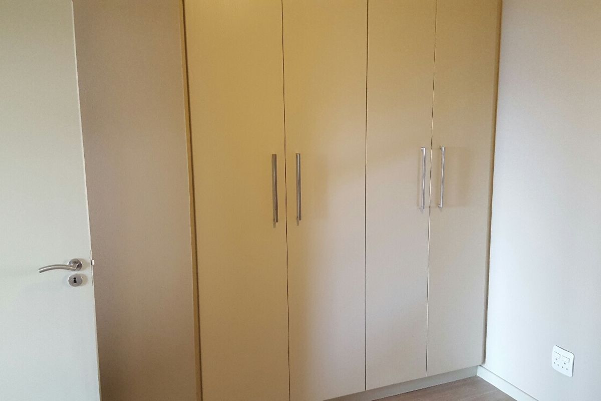 A clean bedroom interior featuring neutral-toned built-in wardrobes with modern handles and a standard internal door.