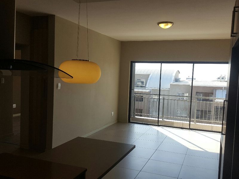 An open-plan living area featuring tiled floors, modern pendant lighting, and large sliding glass doors leading to a balcony with urban views.