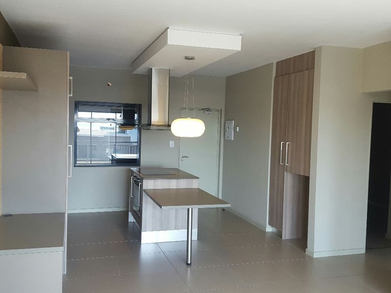 Modern open-plan kitchen area featuring a central island with built-in oven, cooktop, extractor fan, and neutral cabinetry with tiled flooring throughout.