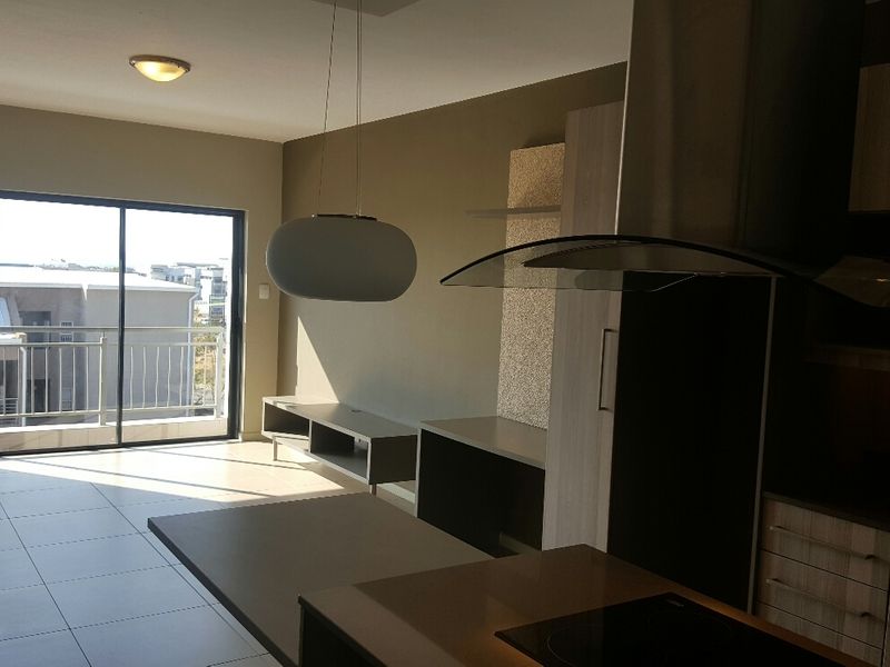 Modern open-plan living area featuring a sleek kitchen with built-in cabinetry, hob, and extractor, flowing onto a private balcony with sliding glass doors.