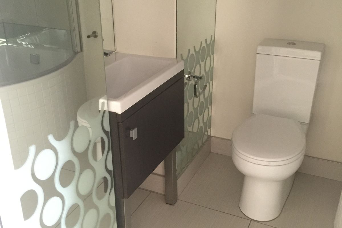 A modern bathroom featuring a wall-mounted vanity with a basin, a toilet, and a glass shower enclosure with decorative frosted detailing.