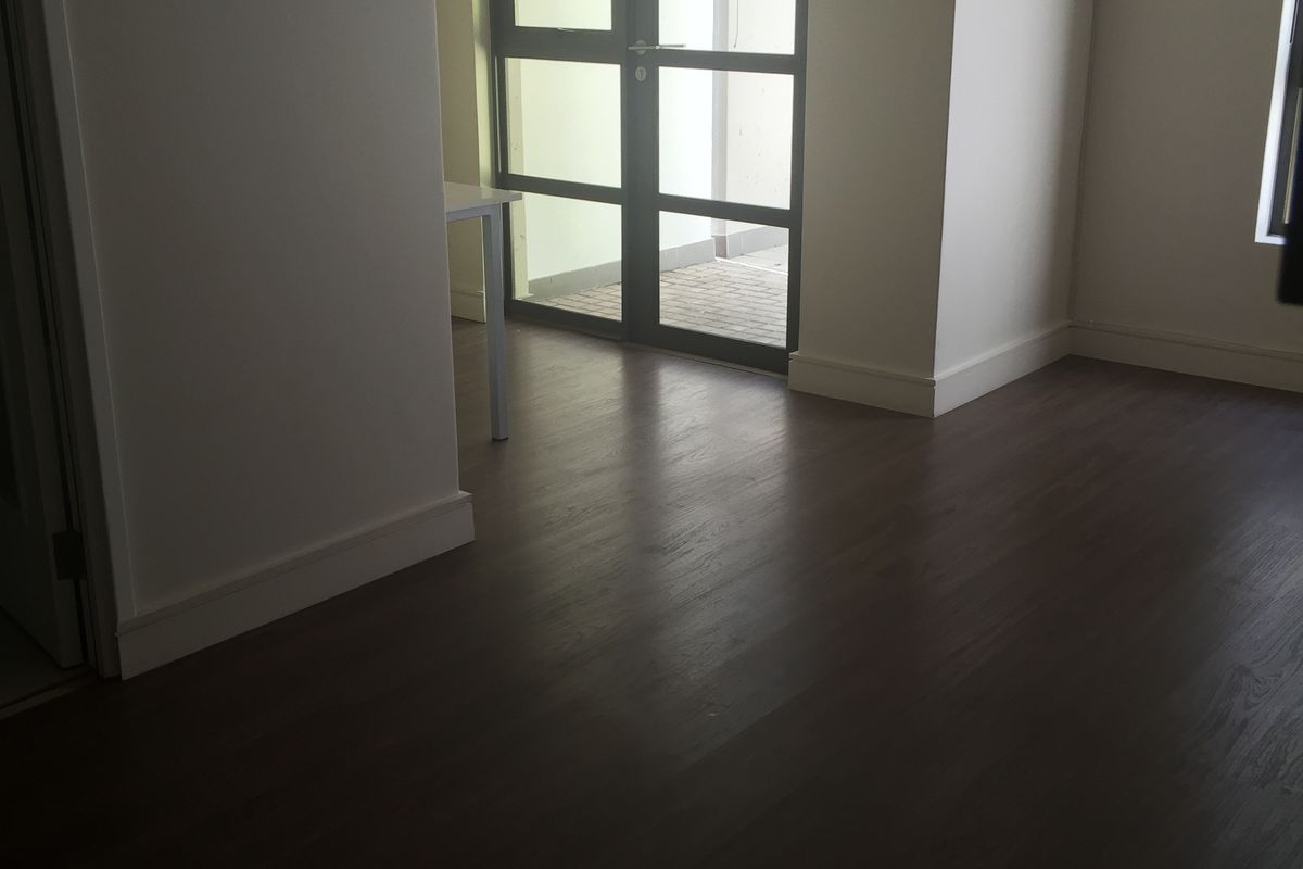 A bright, empty room featuring dark wood-look flooring and a large window with a view, providing a clean and versatile living space.