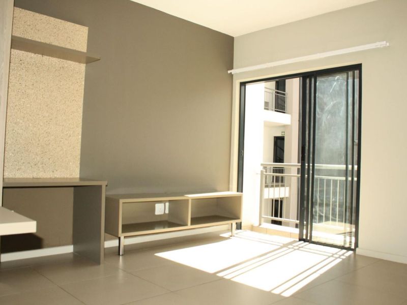 A bright, open-plan living area featuring neutral tiled floors, built-in shelving, and a sliding glass door leading to a private balcony.