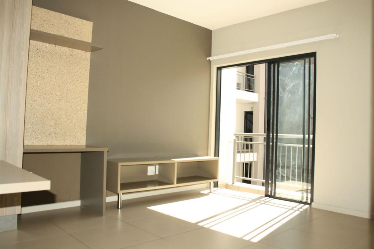 A bright, open-plan living area featuring neutral tiled floors, built-in shelving, and a sliding glass door leading to a private balcony.