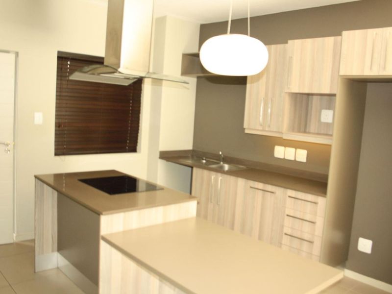 Modern kitchen featuring light wood cabinetry, stone countertops, a built-in electric hob with extractor fan, and tiled flooring.