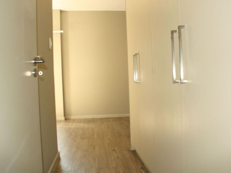 A clean, modern hallway featuring light-toned laminate flooring and ample built-in cupboard storage with sleek metal handles.