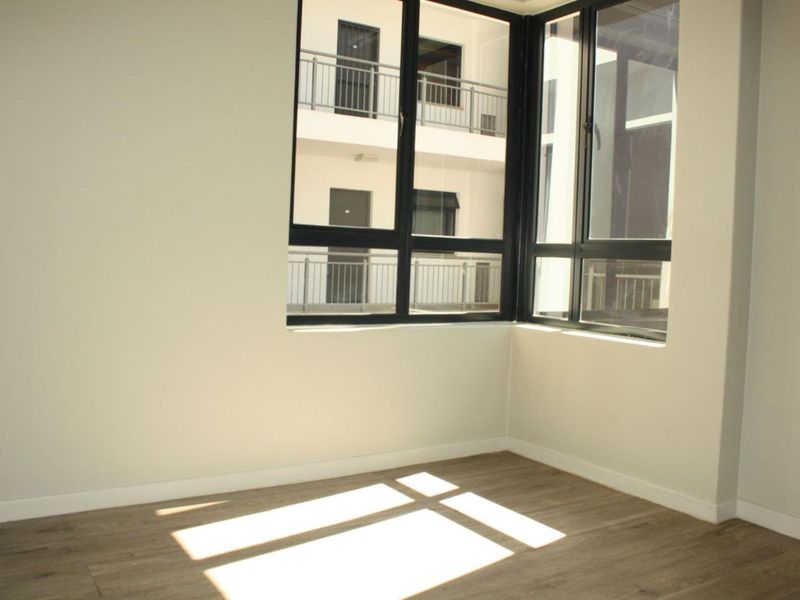 A bright, empty bedroom featuring modern laminate flooring and a large corner window that allows for ample natural light.