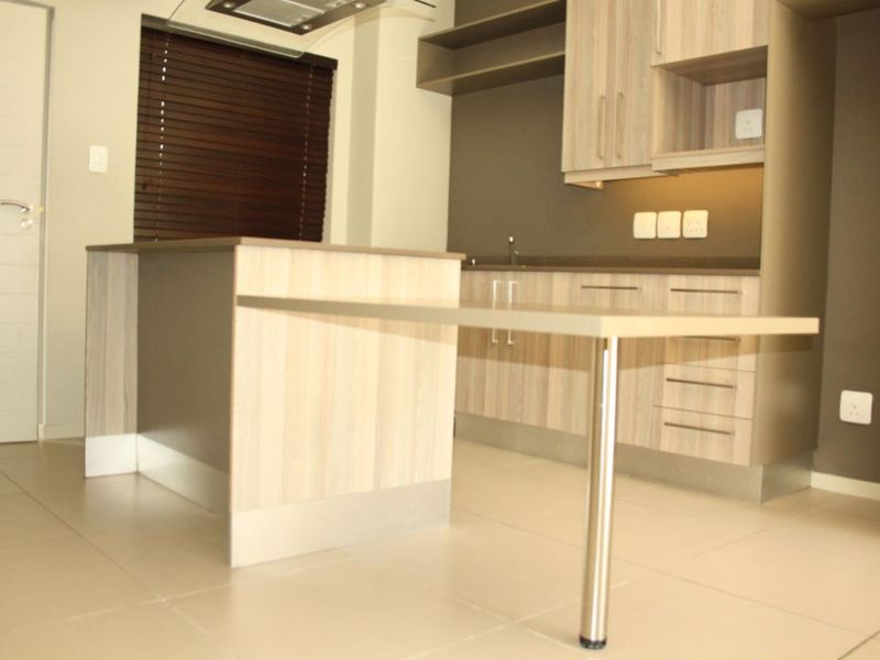 Modern kitchen featuring light wood-finish cabinetry, a functional island with an integrated breakfast bar, and neutral tiled flooring.