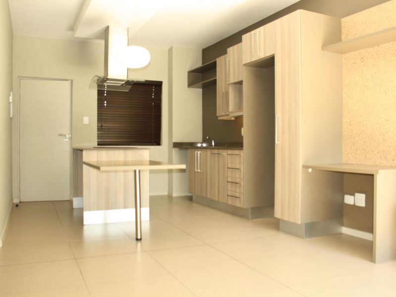 Modern kitchen featuring light wood-finish cabinetry, a central island, integrated shelving, and tiled flooring in an open-plan layout.