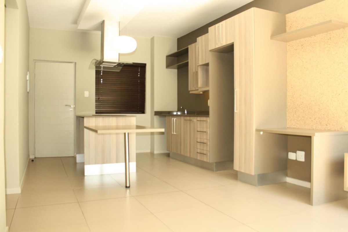 Modern kitchen featuring light wood-finish cabinetry, a central island, integrated shelving, and tiled flooring in an open-plan layout.