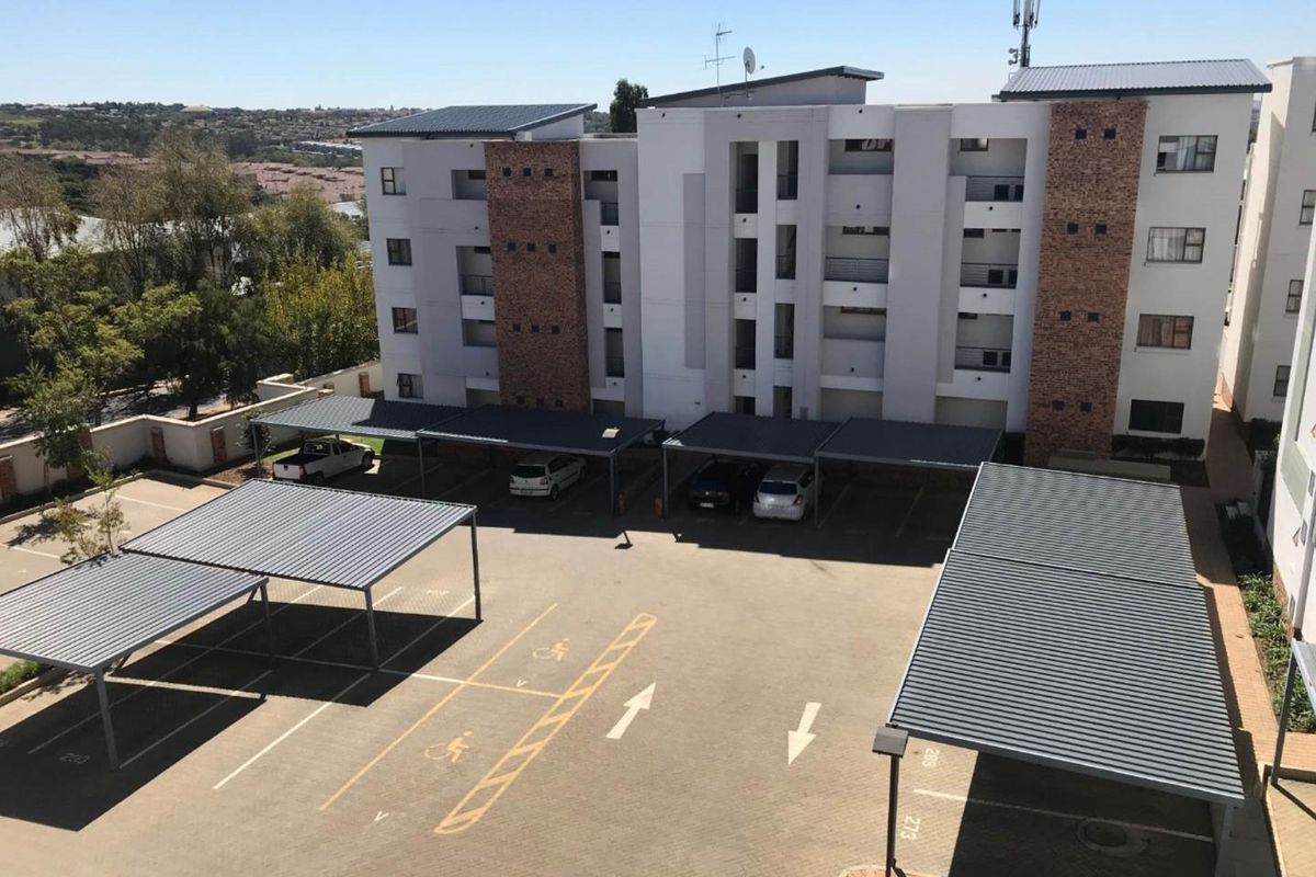 Aerial view of the apartment complex exterior, featuring paved parking areas with covered carports and multi-story residential building facade.