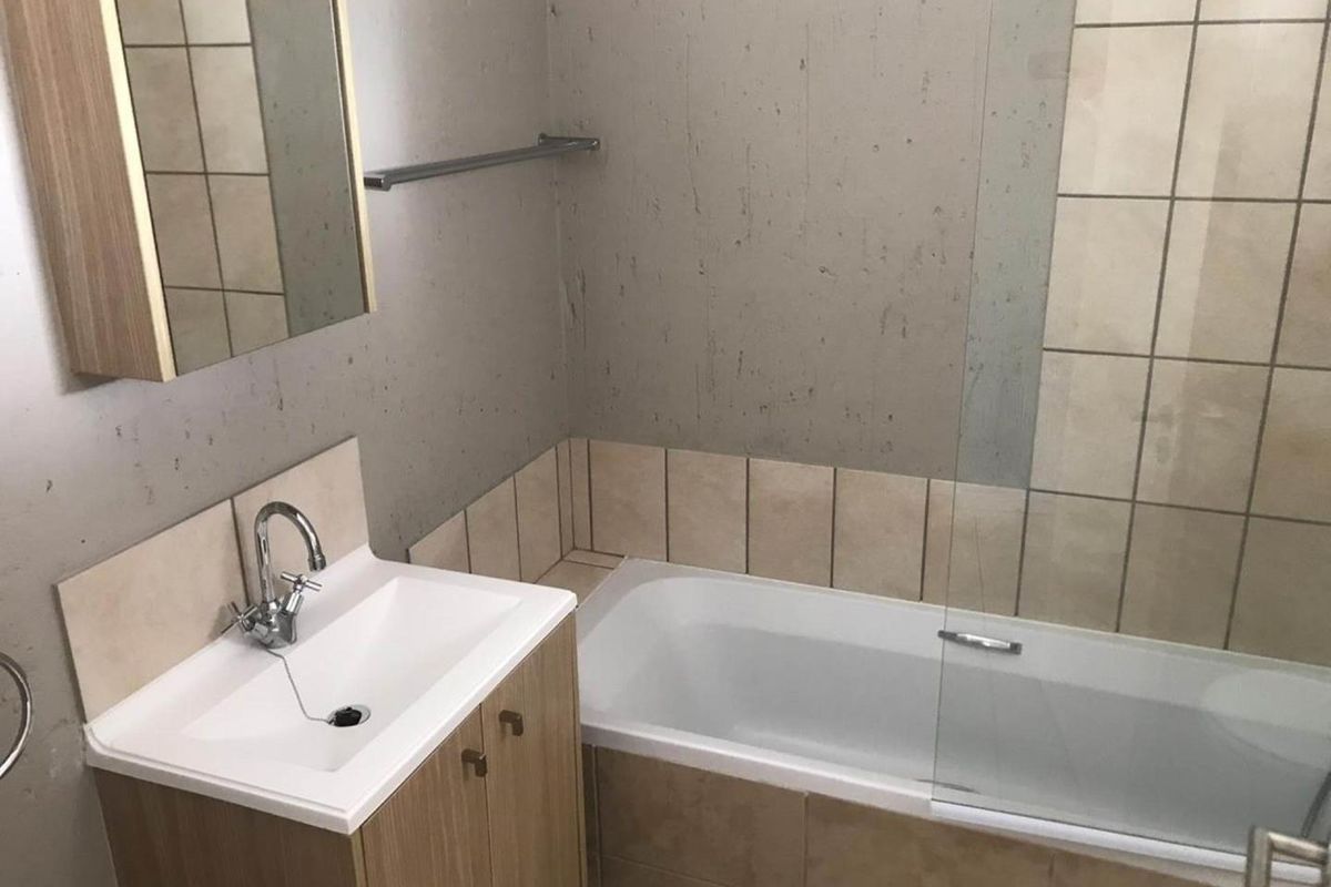 A functional bathroom featuring a vanity cabinet with integrated basin, a bathtub with a glass shower screen, and tiled splashbacks.