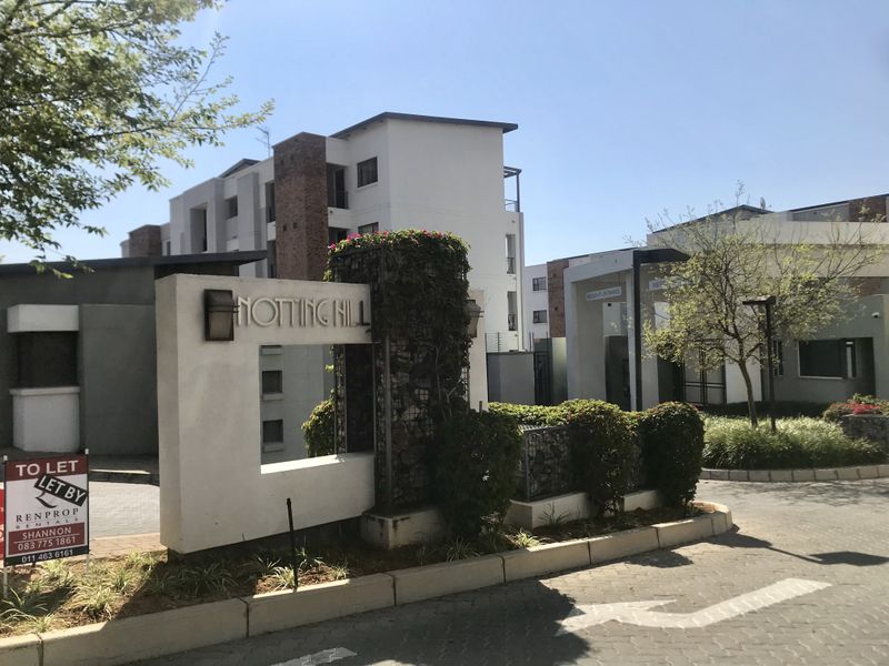 The entrance to Notting Hill apartment complex featuring a modern stone-clad signage pillar, paved driveway, and secure gated access point.