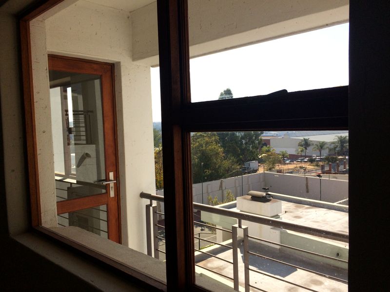 View from an interior room looking out onto a balcony with timber-framed doors and windows and a metal balustrade.