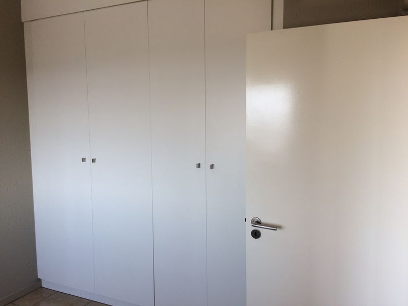 A clean, empty bedroom featuring white built-in cupboards and a modern internal door.