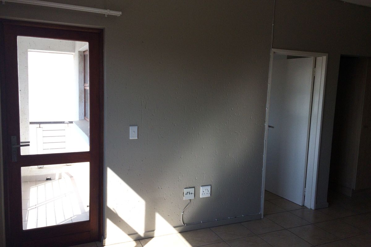 An empty living area featuring tiled flooring, a timber-framed glass door leading to a balcony, and visible surface-mounted electrical conduit.