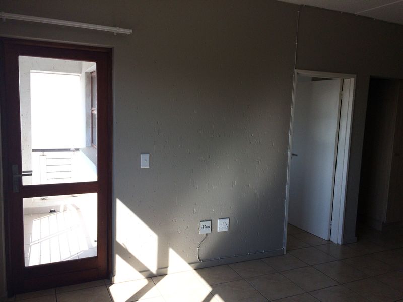 An empty living area featuring tiled flooring, a timber-framed glass door leading to a balcony, and visible surface-mounted electrical conduit.