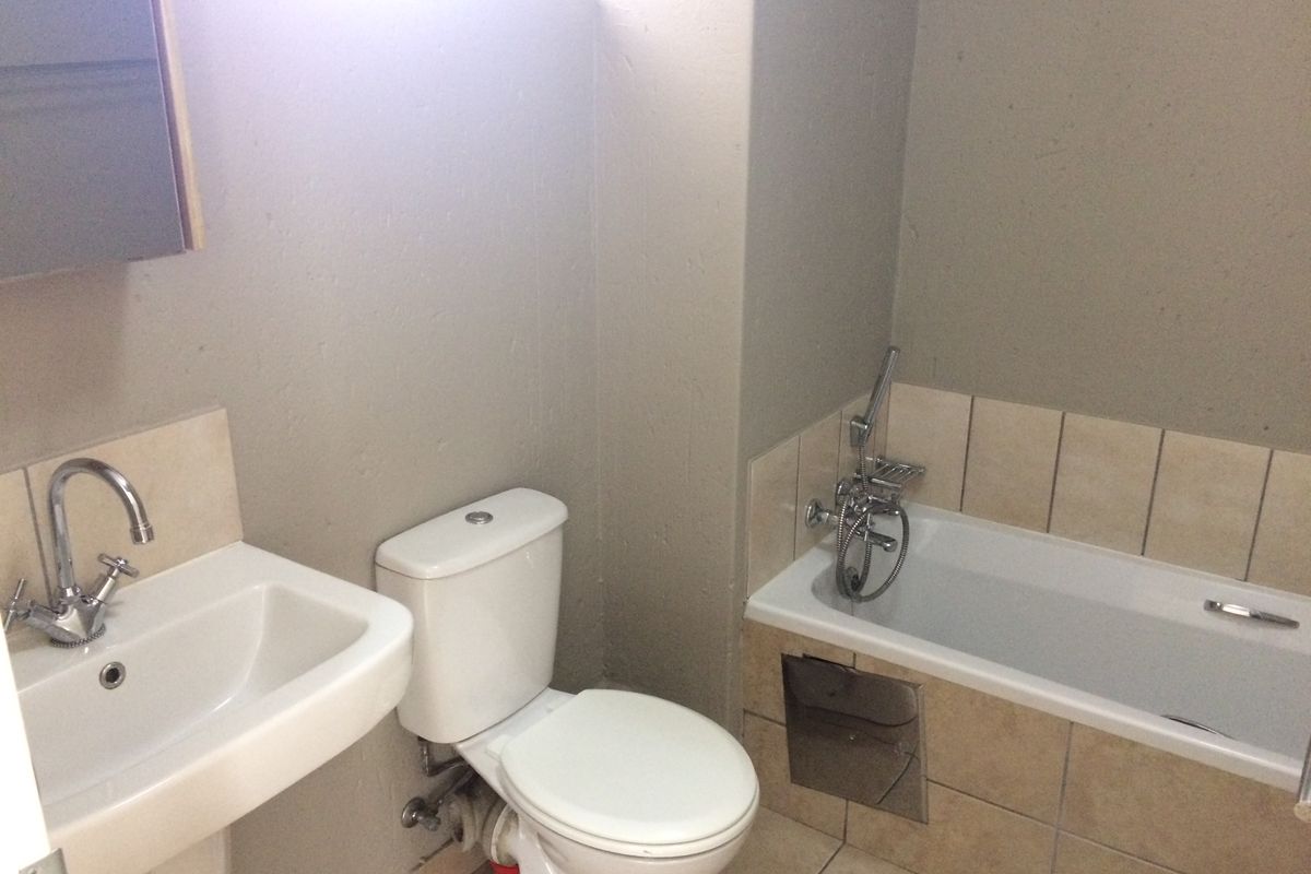 A functional bathroom featuring a pedestal basin, standard toilet, and a built-in bathtub with a chrome shower mixer and tiled surround.