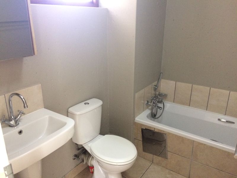A functional bathroom featuring a pedestal basin, standard toilet, and a built-in bathtub with a chrome shower mixer and tiled surround.