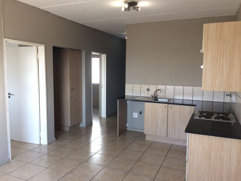 A functional kitchen area featuring light wood-finish cabinetry, dark countertops, a built-in hob, and tiled flooring, currently vacant and ready for updates.